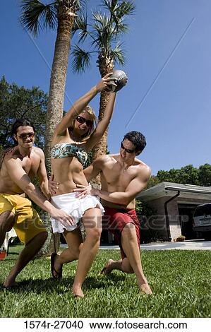 Stock Image - Cheerful friends playing touch football on lawn. Fotosearch