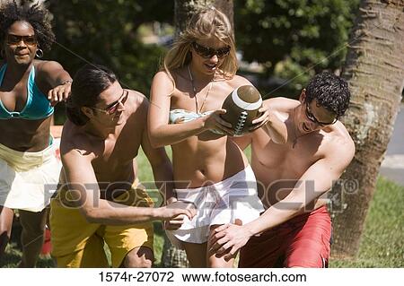 Stock Image - Cheerful friends playing touch football on lawn. Fotosearch