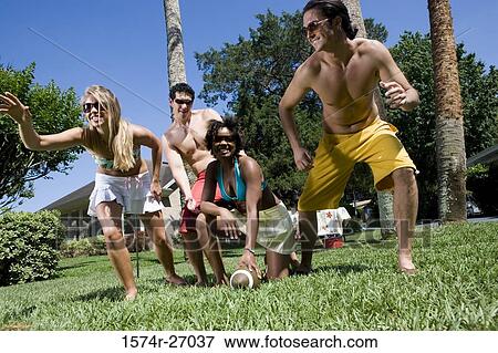 Stock Photo - Cheerful friends playing touch football on lawn. Fotosearch