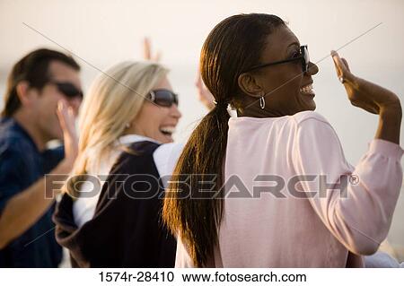 Cheerful friends waving while looking away View Large Photo Image Stock Image - Cheerful friends waving while looking away. Fotosearch