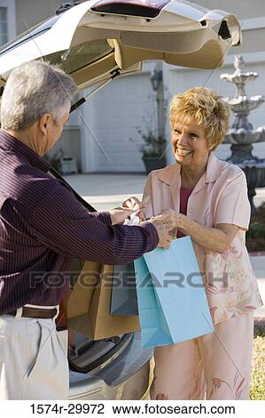 Stock Image - Cheerful mature couple standing together with shopping bags. Fotosearch