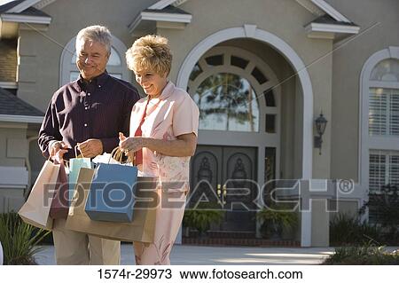 Stock Image - Cheerful mature couple standing together with shopping bags. Fotosearch