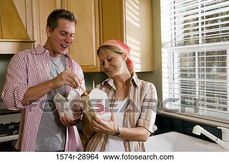 Cheerful mid adult couple eating fast food in the kitchen View Large Photo Image Picture - Cheerful mid adult couple eating fast food in the kitchen. Fotosearch