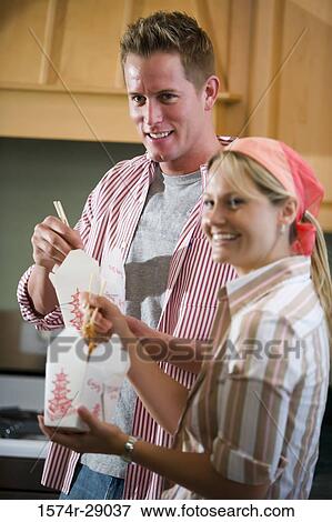 Cheerful mid adult couple eating noodles in the kitchen View Large Photo Image Stock Photo - Cheerful mid adult couple eating noodles in the kitchen. Fotosearch