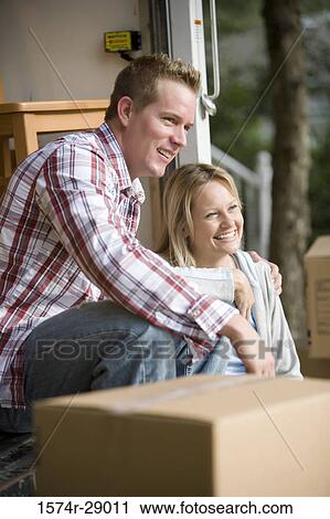 Stock Image - Cheerful mid adult couple sitting by a moving van. Fotosearch
