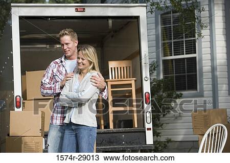 Stock Image - Cheerful mid adult couple sitting by a moving van. Fotosearch