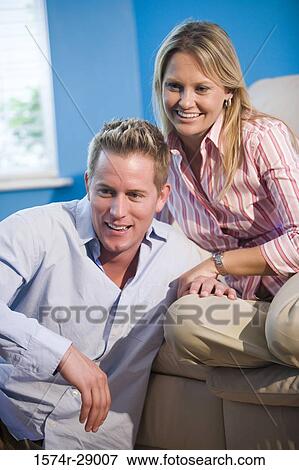 Cheerful mid adult couple sitting on a sofa View Large Photo Image Stock Photo - Cheerful mid adult couple sitting on a sofa. Fotosearch