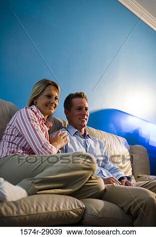 Cheerful mid adult couple sitting on a sofa View Large Photo Image Stock Photo - Cheerful mid adult couple sitting on a sofa. Fotosearch