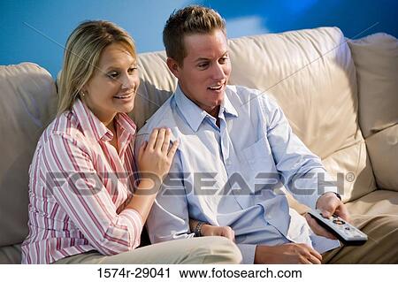 Cheerful mid adult couple with remote control sitting on a sofa View Large Photo Image Stock Image - Cheerful mid adult couple with remote control sitting on a sofa. Fotosearch