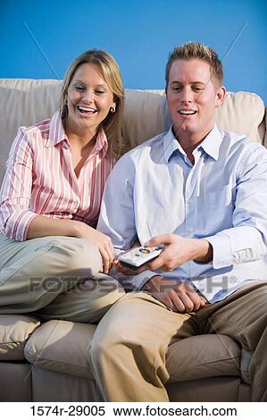 Cheerful mid adult couple with remote control sitting on a sofa View Large Photo Image Stock Photography - Cheerful mid adult couple with remote control sitting on a sofa. Fotosearch