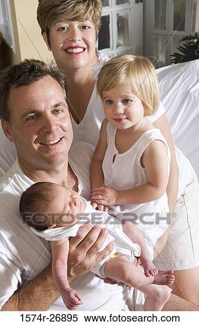 Stock Photography - Cheerful mid adult man and woman holding baby and daughter. Fotosearch