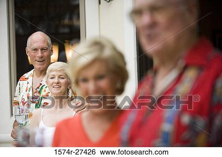 Stock Photograph - Cheerful senior people standing outside house and holding wineglass. Fotosearch