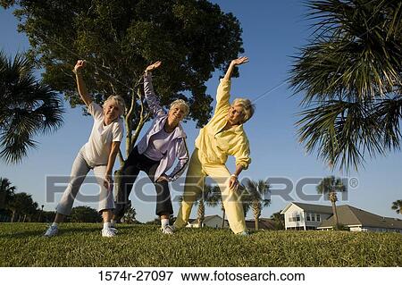 Cheerful senior woman exercising on grass with hand on knee and arms raised View Large Photo Image Stock Photo - Cheerful senior woman exercising on grass with hand on knee and arms raised. Fotosearch