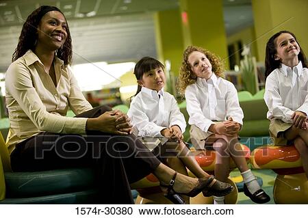 Cheerful teacher sitting with schoolgirls in the library View Large Photo Image Stock Image - Cheerful teacher sitting with schoolgirls in the library. Fotosearch
