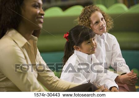 Cheerful teacher sitting with schoolgirls and looking away View Large Photo Image Stock Image - Cheerful teacher sitting with schoolgirls and looking away. Fotosearch