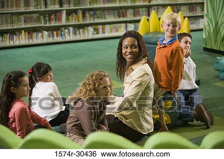 Cheerful teacher sitting with students and looking over shoulder View Large Photo Image Stock Photograph - Cheerful teacher sitting with students and looking over shoulder. Fotosearch