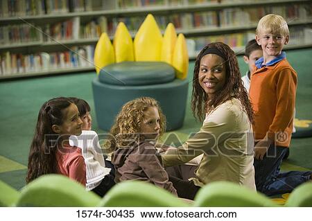 Cheerful teacher sitting with students and looking over shoulder View Large Photo Image Stock Photography - Cheerful teacher sitting with students and looking over shoulder. Fotosearch
