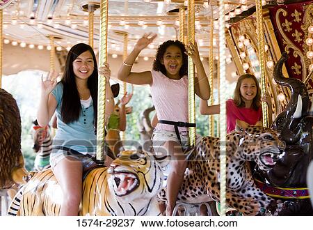 Cheerful teenage girls sitting on a carousel and waving hands View Large Photo Image Stock Photo - Cheerful teenage girls sitting on a carousel and waving hands. Fotosearch