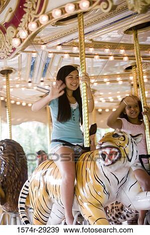 Cheerful teenage girls sitting on a carousel and waving hands View Large Photo Image Stock Photo - Cheerful teenage girls sitting on a carousel and waving hands. Fotosearch