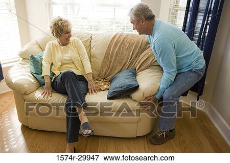 Stock Photo - Cheerful woman sitting while a man holding a couch. Fotosearch