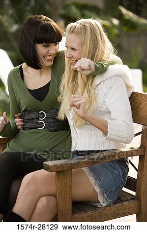 Stock Photo - Cheerful women sitting on armchairs by wall. Fotosearch