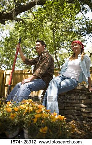Cheerful young couple sitting on stone wall at front or back yard View Large Photo Image Stock Image - Cheerful young couple sitting on stone wall at front or back yard. Fotosearch