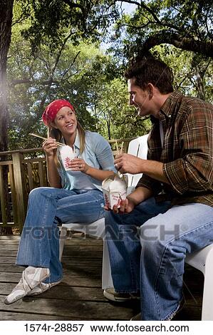 Cheerful young couple sitting together on armchairs and eating View Large Photo Image Stock Photo - Cheerful young couple sitting together on armchairs and eating. Fotosearch