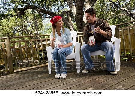 Stock Photography - Cheerful young couple sitting together on armchairs and eating. Fotosearch