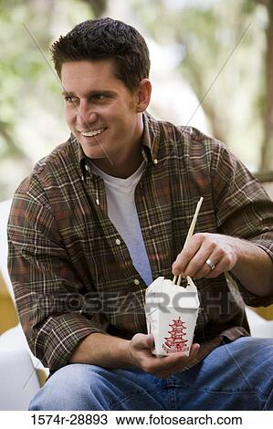 Stock Image - Cheerful young man holding chopsticks and box. Fotosearch