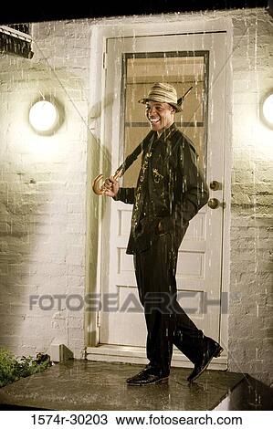 Cheerful young man standing in front of the door and holding an umbrella View Large Photo Image Stock Image - Cheerful young man standing in front of the door and holding an umbrella. Fotosearch