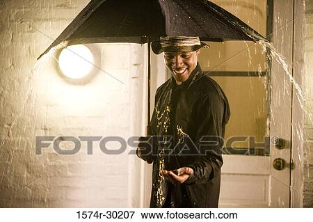 Cheerful young man standing under an umbrella in the rain View Large Photo Image Stock Photo - Cheerful young man standing under an umbrella in the rain. Fotosearch
