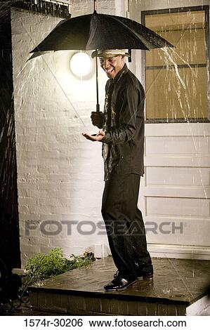 Cheerful young man standing under an umbrella in the rain View Large Photo Image Stock Photograph - Cheerful young man standing under an umbrella in the rain. Fotosearch