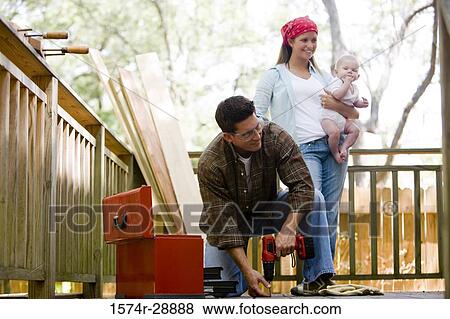 Cheerful young woman holding baby while young man by toolbox View Large Photo Image Stock Photo - Cheerful young woman holding baby while young man by toolbox. Fotosearch