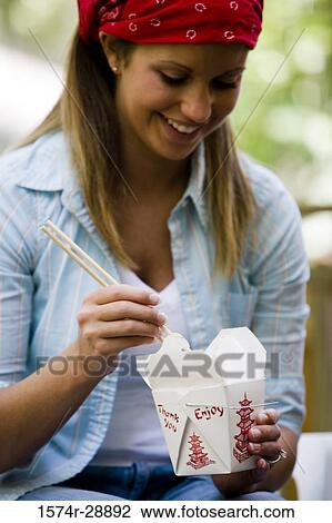 Stock Image - Cheerful young woman holding chopsticks and box. Fotosearch
