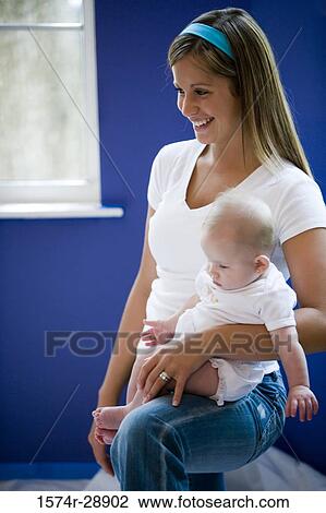 Stock Image - Cheerful young woman holding her baby on her lap. Fotosearch