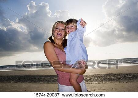 Cheerful young woman holding her son at the beach View Large Photo Image Stock Photo - Cheerful young woman holding her son at the beach. Fotosearch