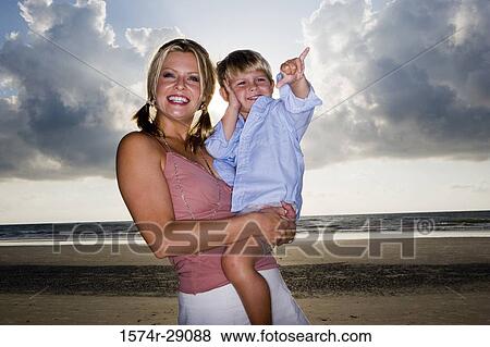 Cheerful young woman holding her son at the beach View Large Photo Image Stock Photo - Cheerful young woman holding her son at the beach. Fotosearch
