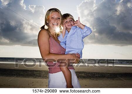 Cheerful young woman holding her son at the beach View Large Photo Image Stock Photo - Cheerful young woman holding her son at the beach. Fotosearch
