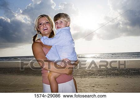 Cheerful young woman holding her son at the beach View Large Photo Image Stock Photograph - Cheerful young woman holding her son at the beach. Fotosearch