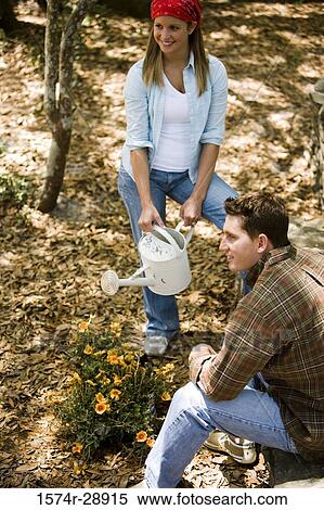 Cheerful young woman holding watering can while young man sitting beside View Large Photo Image Stock Photography - Cheerful young woman holding watering can while young man sitting beside. Fotosearch