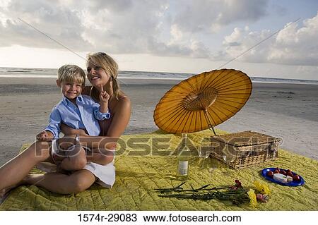 Cheerful young woman sitting with her son at the beach View Large Photo Image Stock Image - Cheerful young woman sitting with her son at the beach. Fotosearch