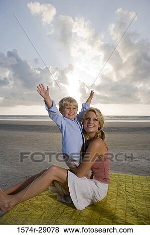 Cheerful young woman sitting with her son at the beach View Large Photo Image Stock Photo - Cheerful young woman sitting with her son at the beach. Fotosearch