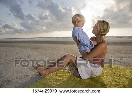 Cheerful young woman sitting with her son at the beach View Large Photo Image Stock Photo - Cheerful young woman sitting with her son at the beach. Fotosearch