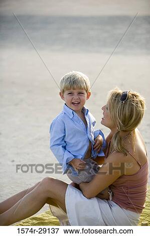 Cheerful young woman sitting with her son at the beach View Large Photo Image Stock Photo - Cheerful young woman sitting with her son at the beach. Fotosearch