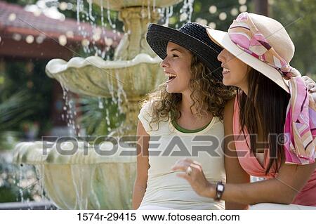 Cheerful young woman sitting with her friend by water fountain View Large Photo Image Stock Photography - Cheerful young woman sitting with her friend by water fountain. Fotosearch