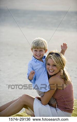 Cheerful young woman sitting with son at the beach View Large Photo Image Stock Photograph - Cheerful young woman sitting with son at the beach. Fotosearch