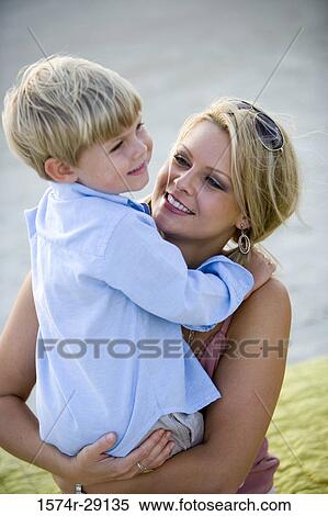 Stock Photography - Cheerful young woman sitting with son at the beach. Fotosearch