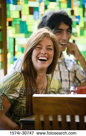 Stock Photo - Cheerful young woman sitting with brother by table. Fotosearch