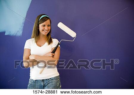 Cheerful young woman with paint roller by wall View Large Photo Image Stock Image - Cheerful young woman with paint roller by wall. Fotosearch