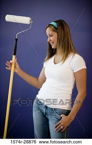 Cheerful young woman with paint roller by wall View Large Photo Image Stock Photograph - Cheerful young woman with paint roller by wall. Fotosearch